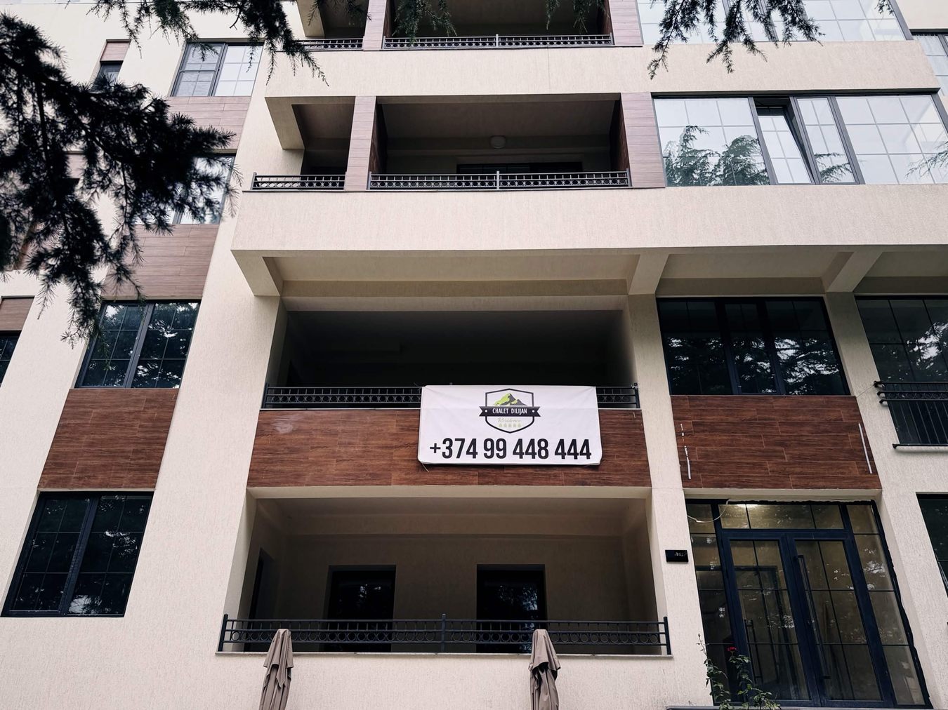 米色新建公寓大樓的陽台上掛著 CHALET DILIJAN Residence 的白色布條廣告，附電話號碼
