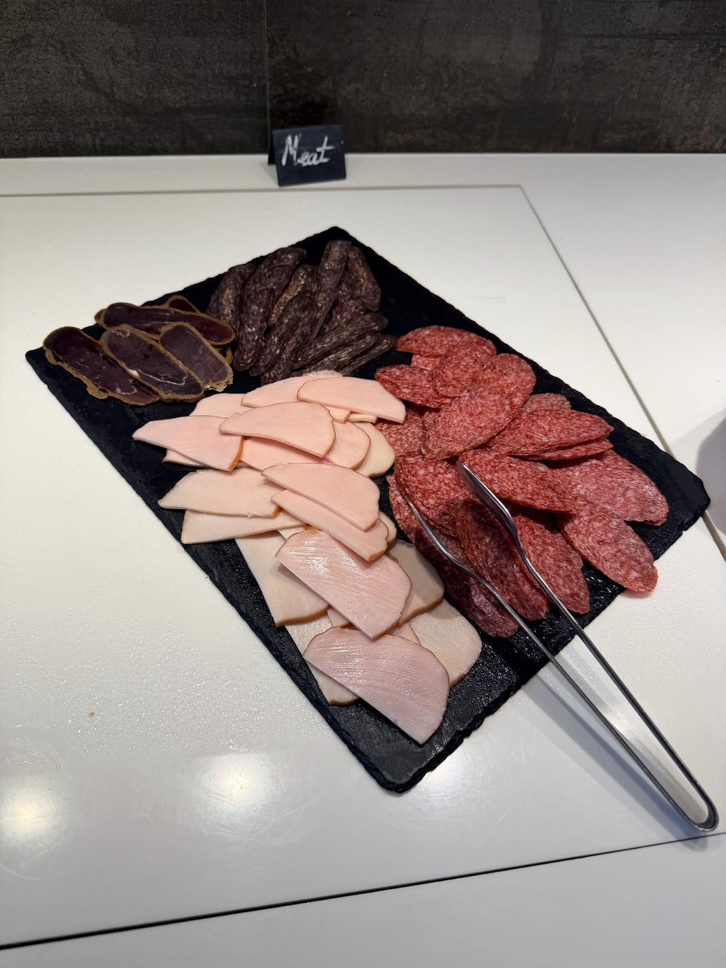 早餐冷肉盤，石板上四種切片：裹香料的 basturma、細長的 sujuk、義式沙拉米、火腿與煙燻雞胸